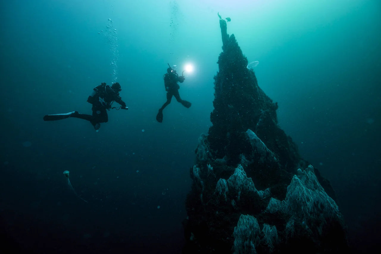 Divers with a light beside a submerged pinnacle in PADI Deep Diver imagery.
