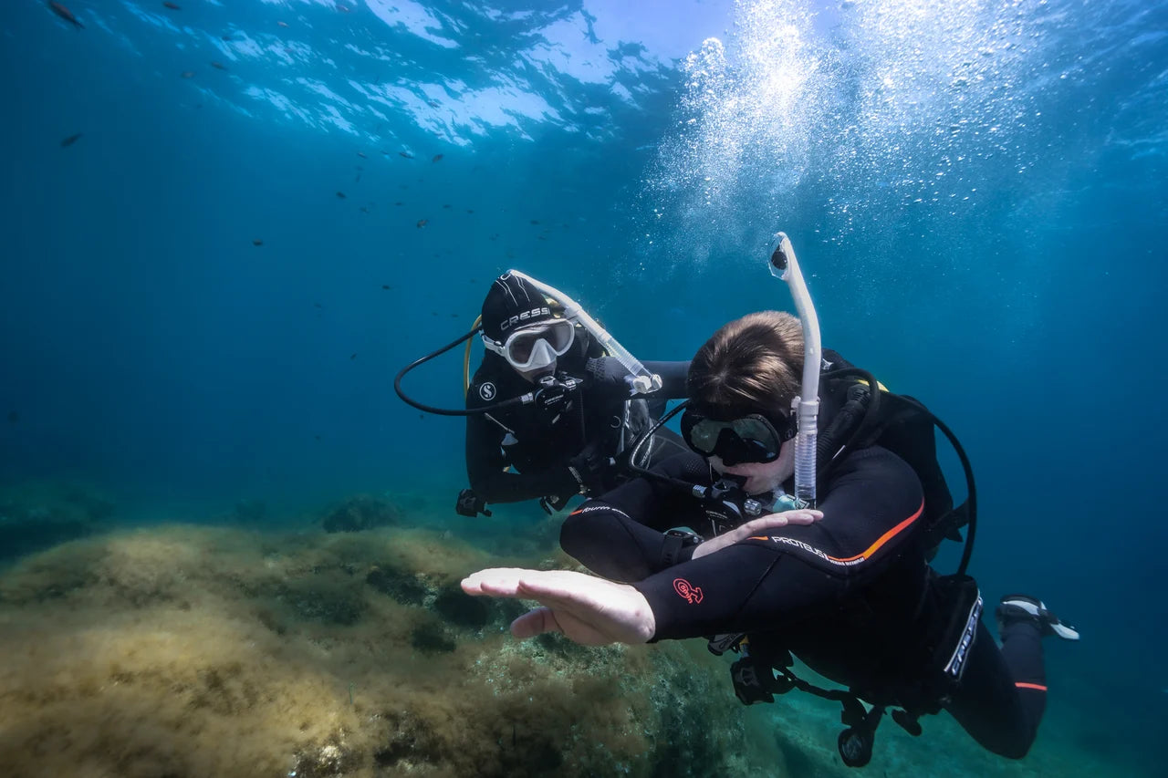 An instructor demonstrates an underwater skill with another diver.