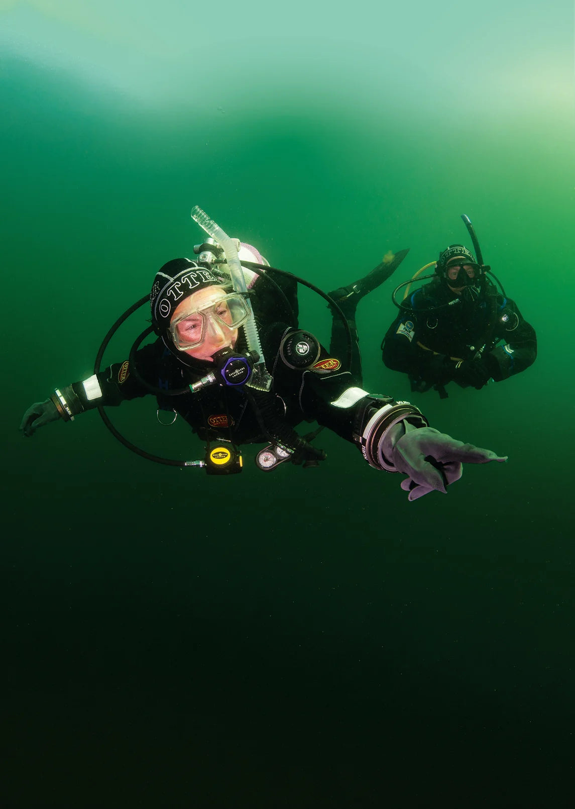 Drysuit divers in green open water. © PADI 2026
